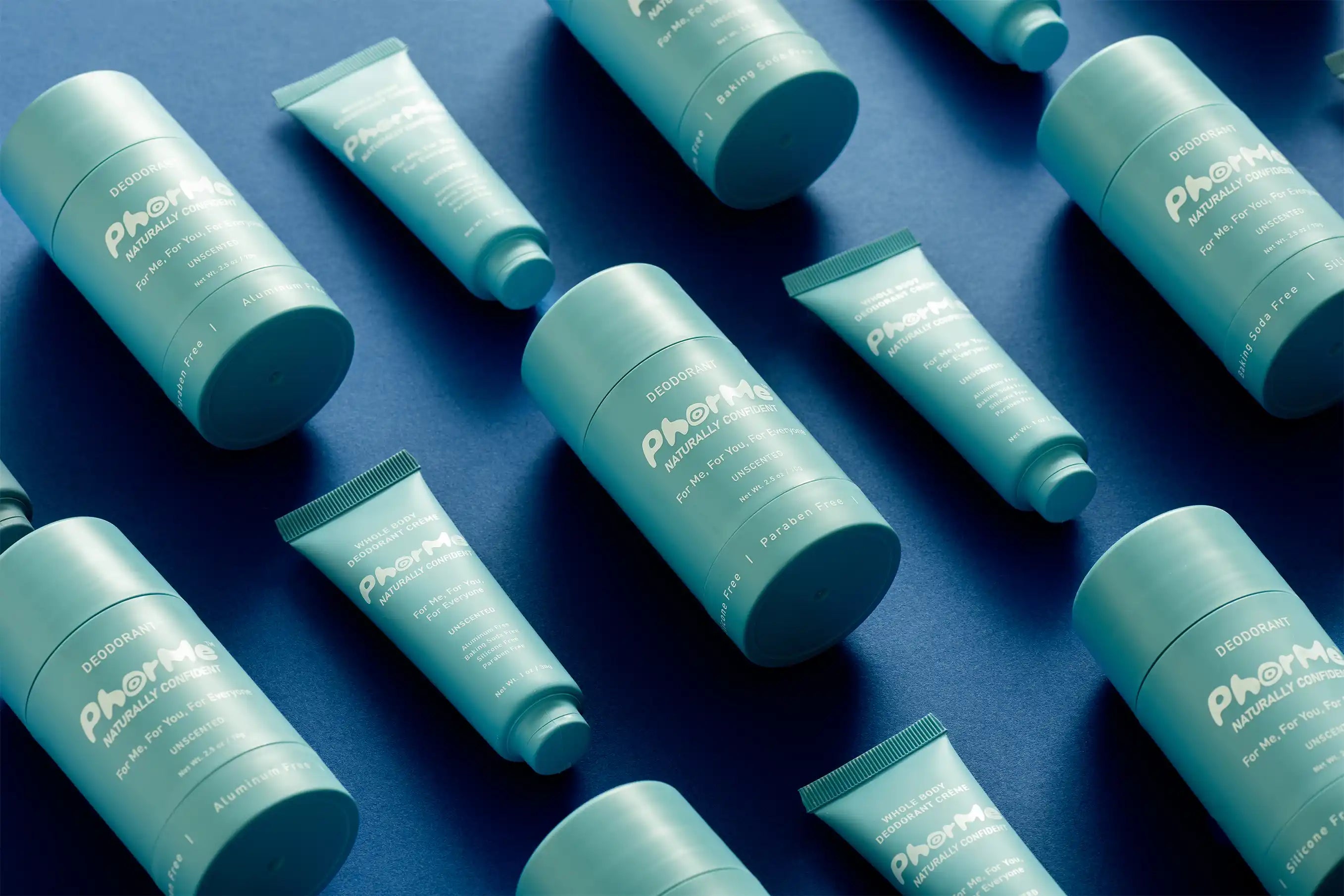 Flat lay of PhorMe unscented natural deodorant sticks and whole body deodorant crèmes arranged diagonally on a deep blue background. Aluminum-free, baking soda-free deodorant designed for all skin types and every body.